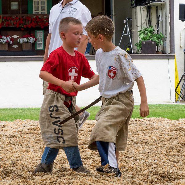 Two boys in burlap Schwingen breeches gripping each other in a ring of sawdust at the club hall